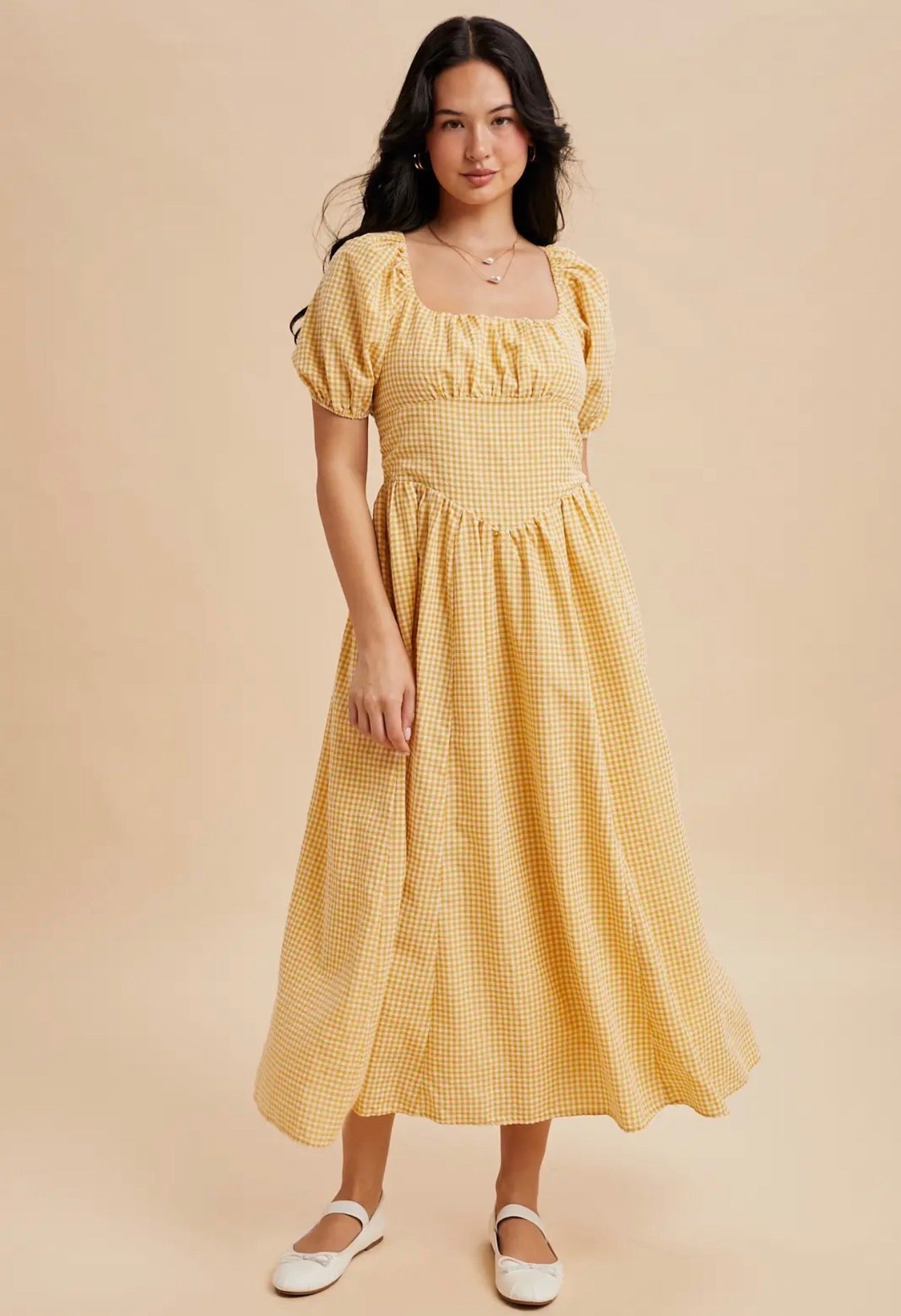Woman wearing a yellow checkered dress against a beige background