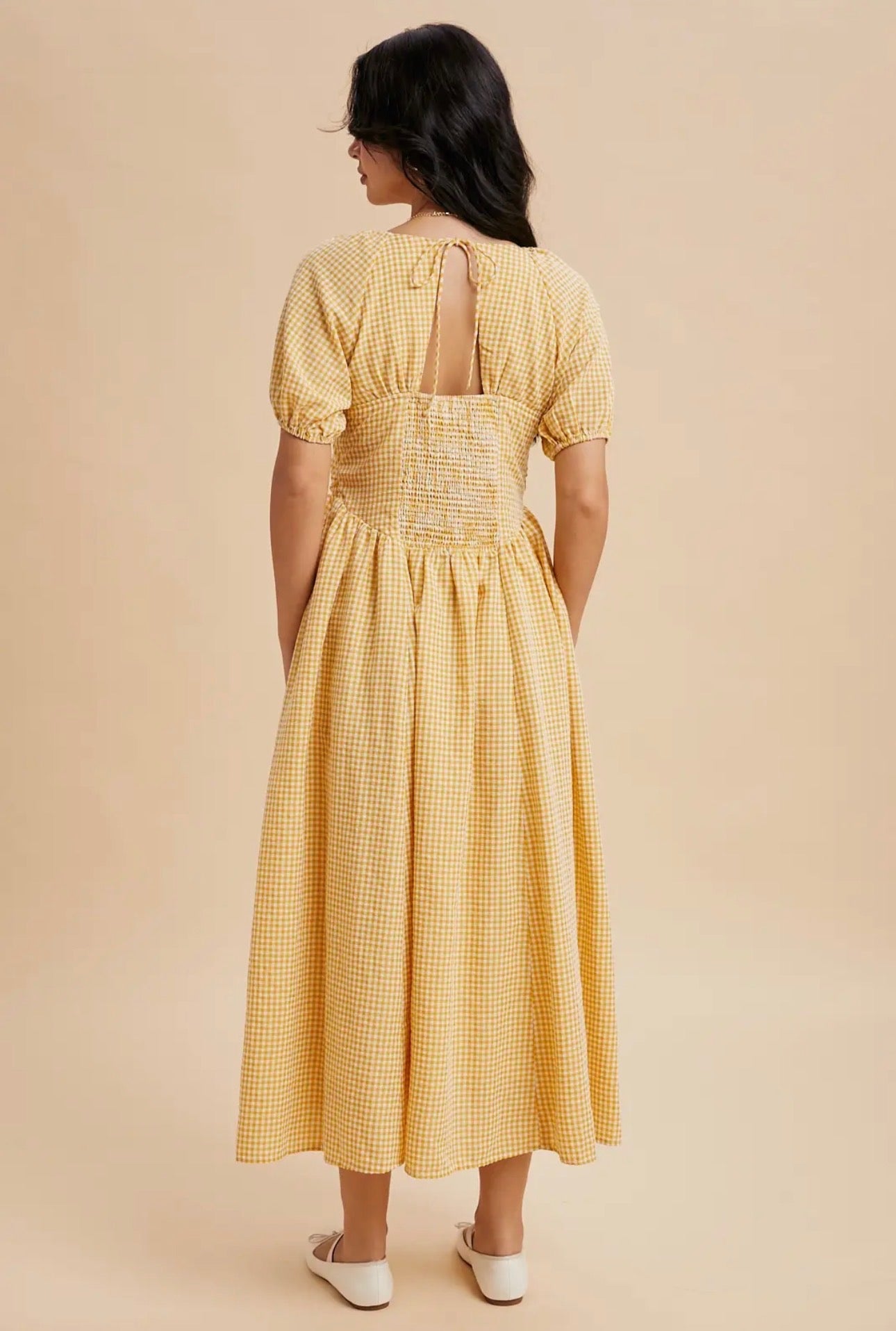 Woman wearing a yellow checkered dress with a cut-out back on a beige background